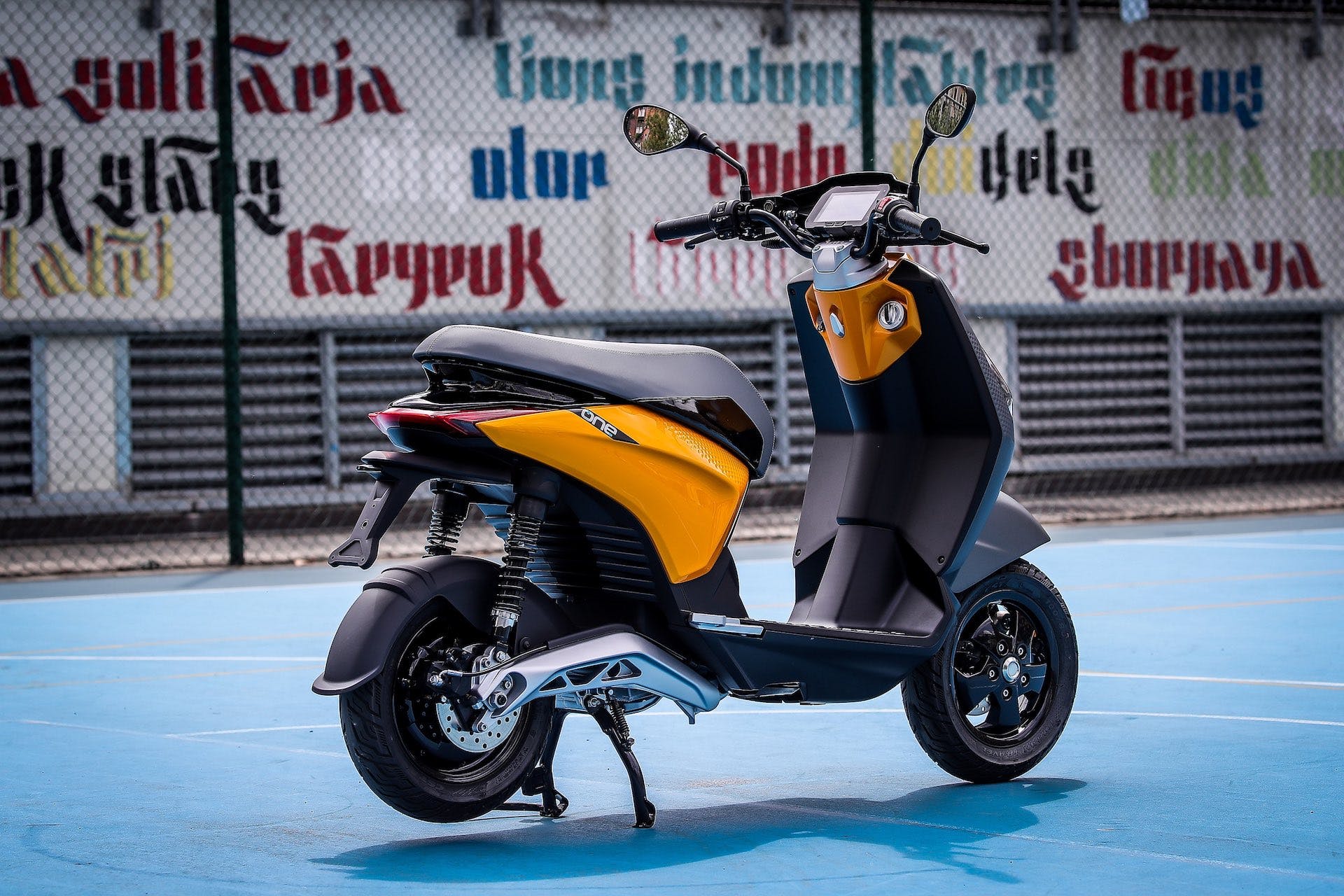 Scooter elettrico Piaggio One, giallo e grigio scuro, fermo su cavalletto e visto di tre quarti posteriormente.